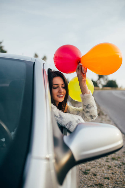 Молодая женщина развлекается, держа воздушные шары через окно машины. Селективный акцент на женской руке. - Фото, изображение