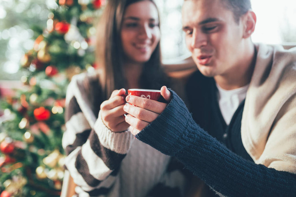 Young couple drinking hot tea together, with a Christmas tree in a background. - Photo, Image