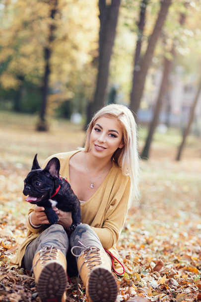 Mujer hermosa y feliz disfrutando en el parque disfrutando con su adorable bulldog francés. Tiempo de otoño
 - Foto, imagen