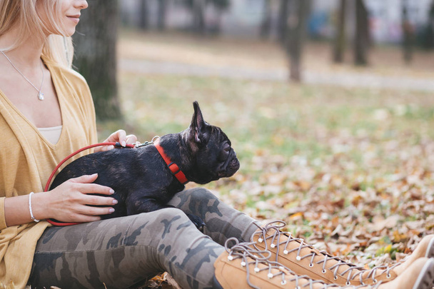 Mooi en gelukkig vrouw genieten in park genieten met haar schattige Franse bulldog. Herfst tijd - Foto, afbeelding