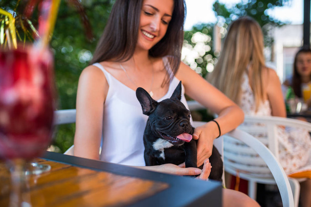 Young woman enjoying in a cafeteria keeping adorable French bulldog puppy  - Fotografie, Obrázek