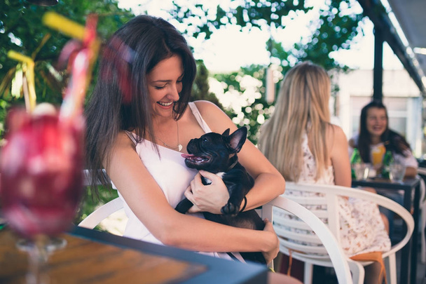 Young woman enjoying in a cafeteria keeping adorable French bulldog puppy  - Foto, Imagem