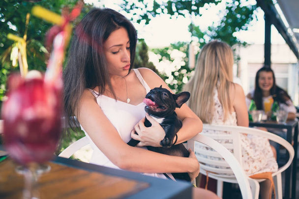 Young woman enjoying in a cafeteria keeping adorable French bulldog puppy  - Photo, image