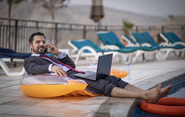hombre árabe de mediana edad trabajando durante sus vacaciones de verano junto a una piscina
 - Foto, imagen