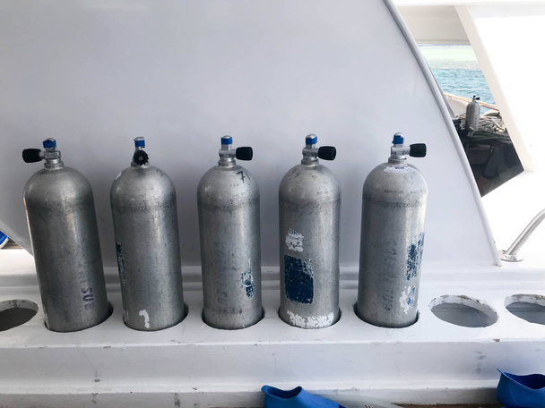 Five large metal, aluminum oxygen bottles for breathing and diving stand on special stands on board a boat, ship, cruise liner, yacht in a tropical seaside summer resort. - Foto, Bild