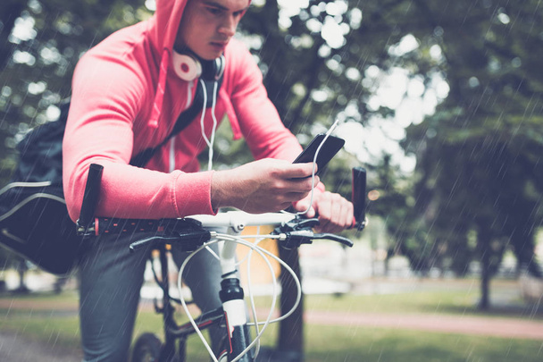 Mann auf Fahrrad in einem Park, während er auf Handy schaut - Foto, Bild