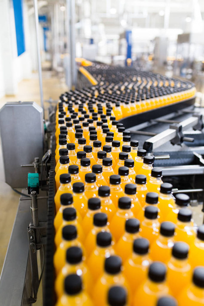 Fabryka przemysłowa wewnątrz i w maszynach. Robotyczna linia fabryczna do przetwarzania i butelkowania butelek z sodą i sokiem pomarańczowym. - Zdjęcie, obraz