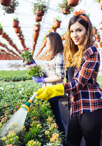 Hermosas mujeres jóvenes trabajando en invernadero y disfrutando en hermosas flores
.  - Foto, imagen