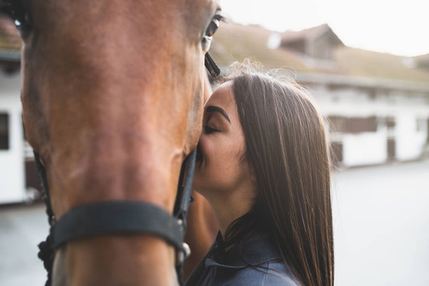 Beautiful brunette girl kissing her horse. Selective focus - Photo, Image