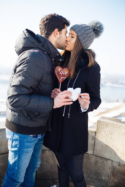 Hermosa pareja joven enamorada disfrutando juntos en la calle de la ciudad y sosteniendo juntos una forma de corazón hecha de nieve
.  - Foto, imagen