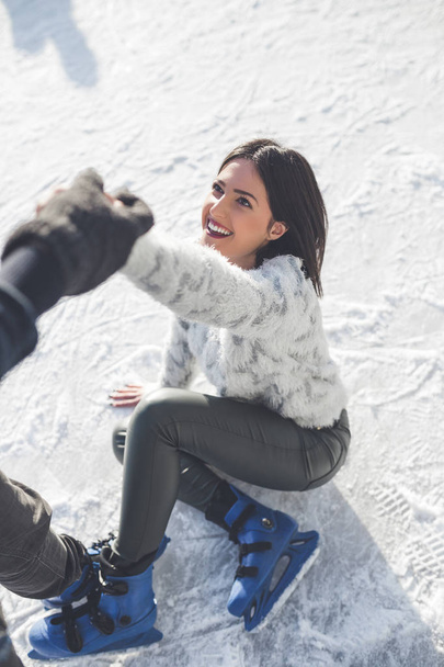 Mulher jovem e bonita desfrutando de patinação no gelo. Ela recebe ajuda após a queda. - Foto, Imagem