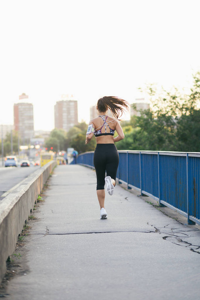 Beautiful athletic woman running outdoors at bridge.  - Фото, изображение