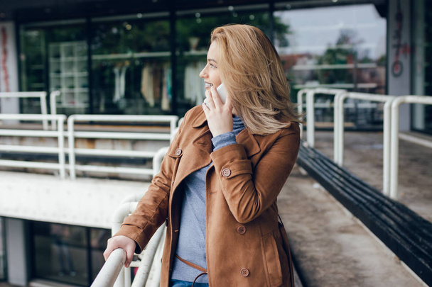 Outdoor portrait of cute happy blonde Caucasian girl  talking on smartphone. - Valokuva, kuva