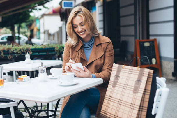 Молодая девушка в кафе пьет кофе и пользуется мобильным телефоном
. - Фото, изображение