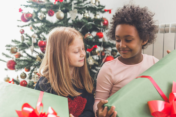Bambine africane e rosse con regali insieme davanti all'albero di Natale. Luce naturale
.  - Foto, immagini