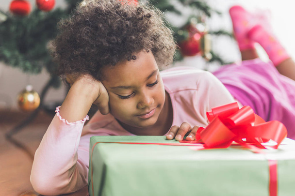 Αφρικανική κοριτσάκι με δώρο μπροστά από το χριστουγεννιάτικο δέντρο. Φυσικό φως.  - Φωτογραφία, εικόνα