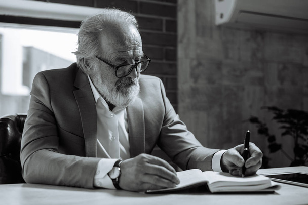 black and white photo. senior man holding pen and writing in notebook - Foto, imagen