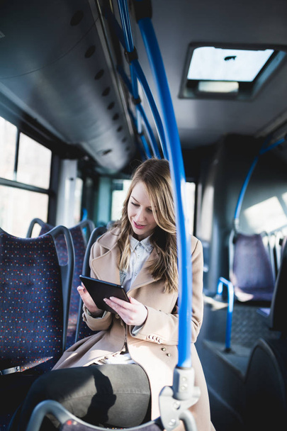 Beautiful young woman smiling, sitting in city bus and looking at tablet.  - Photo, Image