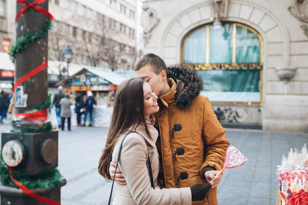 Güzel genç çift birlikte City sokak, sarılma ve kalp şeklinde bir lolipop tutan zevk aşık.  - Fotoğraf, Görsel