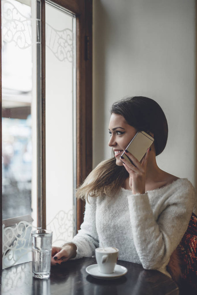 Bella donna seduta da sola in mensa, che beve caffè e parla al cellulare
.  - Foto, immagini