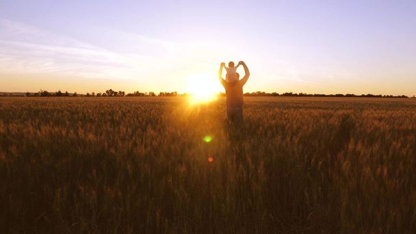 Papá con bebé pequeño bailando y riendo en el fondo de la puesta de sol de oro en el campo con trigo
. - Foto, Imagen