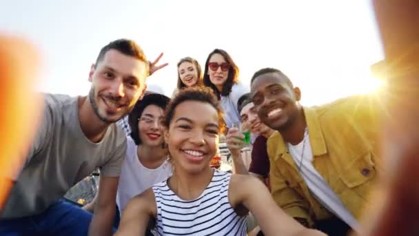 Point de vue de la fille afro-américaine tenant la caméra et prenant selfie avec des amis heureux à la fête sur le toit. Hommes et femmes regardent la caméra, posant et riant
. - Séquence, vidéo