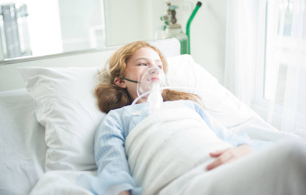 Pieni tyttö on sairas käyttäen happinaamari hänen kasvonsa makaa sängyssä sairaalassa
 - Valokuva, kuva