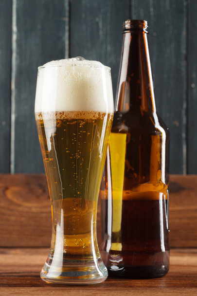 Glass of beer near bottle on wooden background - Foto, imagen
