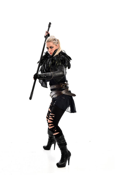 retrato de cuerpo entero de una chica rubia vestida de negro desgarrado, sosteniendo un arma de bastón. pose de pie, aislado sobre fondo blanco del estudio
. - Foto, imagen
