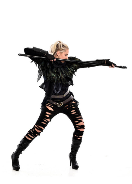 Ganzkörperporträt eines blonden Mädchens im schwarzen zerrissenen Outfit, das eine Dienstwaffe in der Hand hält. Stehende Pose, isoliert auf weißem Studiohintergrund. - Foto, Bild