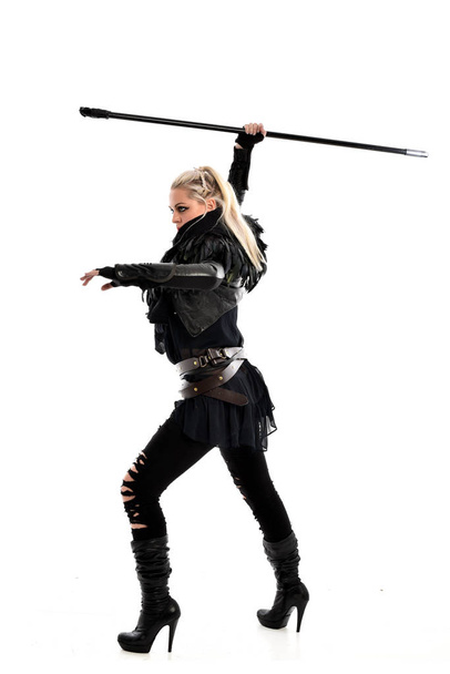 full length portrait of blonde girl wearing black torn outfit, holding a staff weapon. standing pose, isolated on white studio background. - Photo, Image