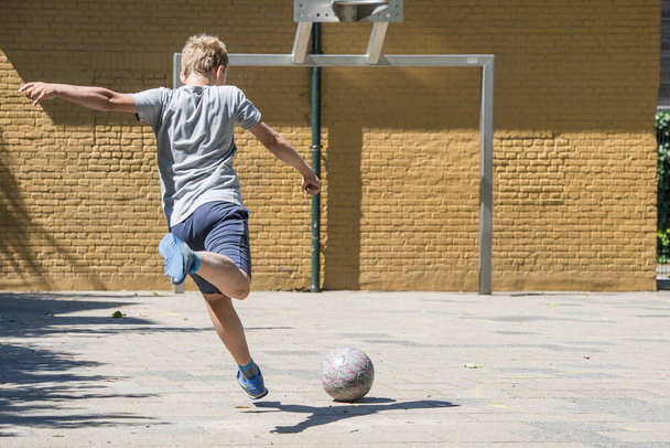 Boy kicking ball towards goal on street soccer pitch - Fotografie, Obrázek
