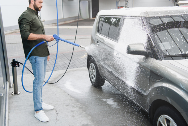 handsome man cleaning car at car wash with high pressure water jet - Photo, image