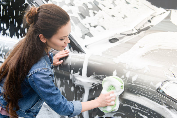vue latérale de la femme attrayante nettoyage de voiture au lavage de voiture avec chiffon et mousse
 - Photo, image