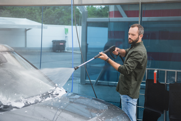 handsome man cleaning car front window at car wash with high pressure water jet - Photo, Image