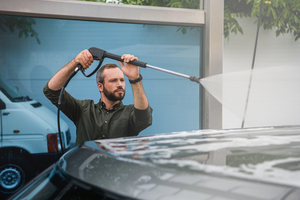 handsome man cleaning car at car wash with high pressure water jet - Foto, Imagem