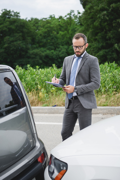 knappe zakenman schrijven iets naar autoverzekering na auto-ongeluk op weg - Foto, afbeelding