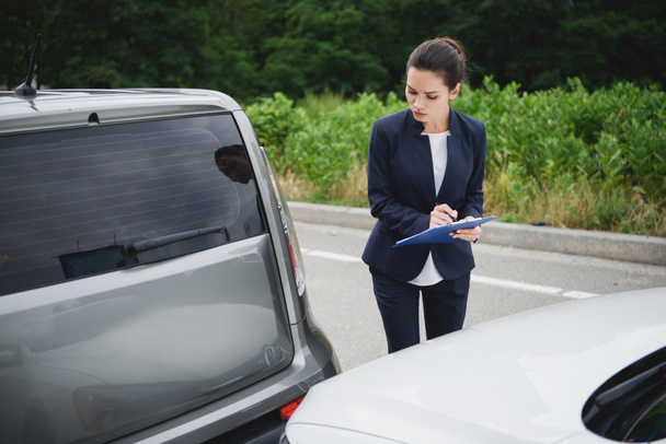 attractive woman writing something to car insurance after car accident - Foto, imagen