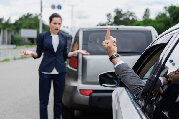 cropped image of driver showing middle finger to businesswoman on road - Photo, Image