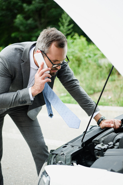 businessman talking by smartphone and looking in open car hood - Photo, Image