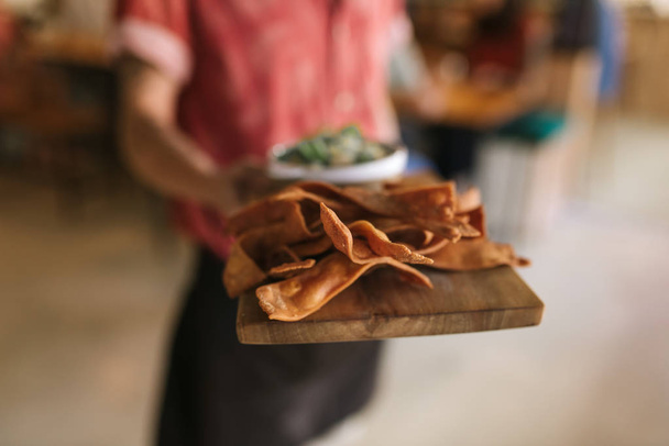 Closeup of a waiter standing in a trendy bistro holding a serving board with freshly made nachos  - Fotoğraf, Görsel