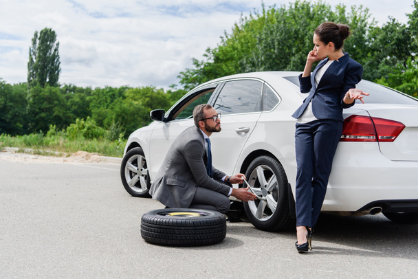 bel homme d'affaires changeant de pneus sur la route, femme d'affaires parlant par smartphone
 - Photo, image