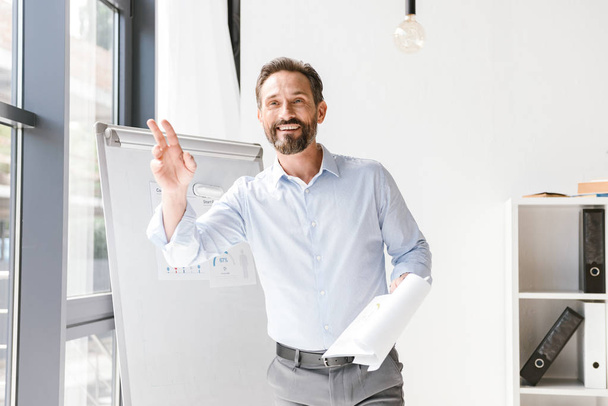 Usmívající se podnikatel pozdrav někoho, když stál v kanceláři s papíry - Fotografie, Obrázek