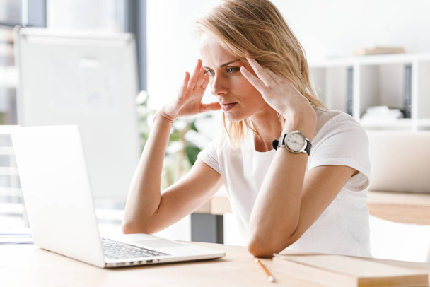 Müde Geschäftsfrau arbeitet am Laptop, während sie am Schreibtisch sitzt - Foto, Bild