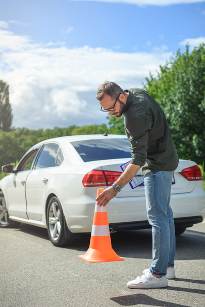 handsome man holding car insurance and putting safety cones on road  - Фото, зображення