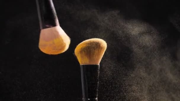 Two Cosmetic brushes with golden cosmetic powder on black background - Séquence, vidéo