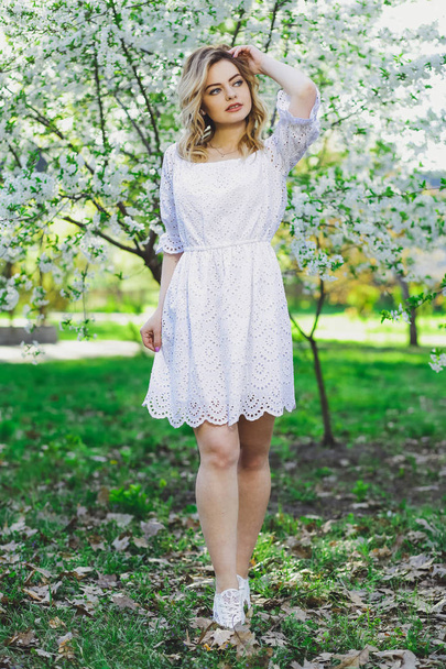 Beautiful blonde girl with blond hair in a dress on a background of spring blooming trees - Фото, зображення