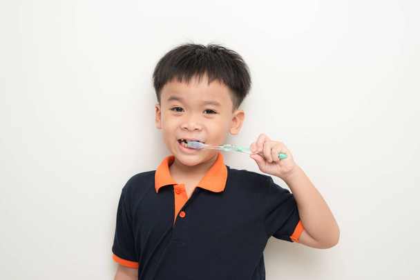 Маленький мальчик чистит зубы стоя на белом фоне
 - Фото, изображение
