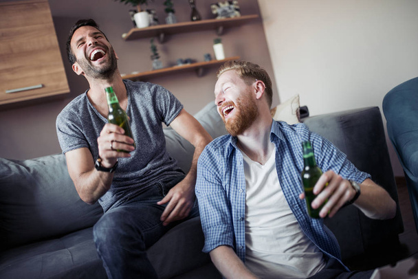 サッカーの試合を見て、家でビールを飲みながら 2 人の男. - 写真・画像