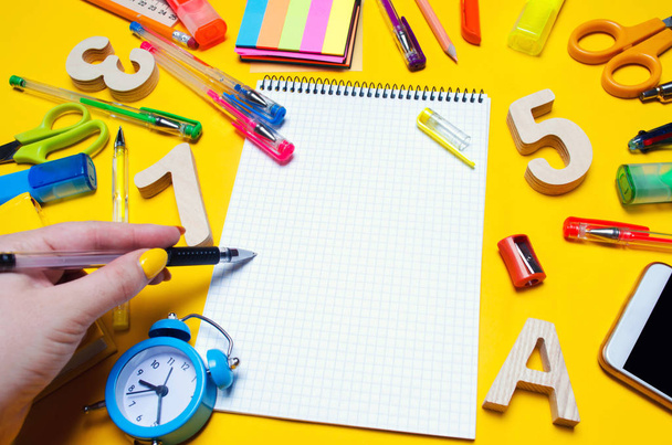 the student makes notes in a notebook. copy space. school accessories on a desk on a yellow background. concept of education. stationery. watches, colored pens, phone, markers. view from above. top view. flat lay. copy space - Foto, afbeelding
